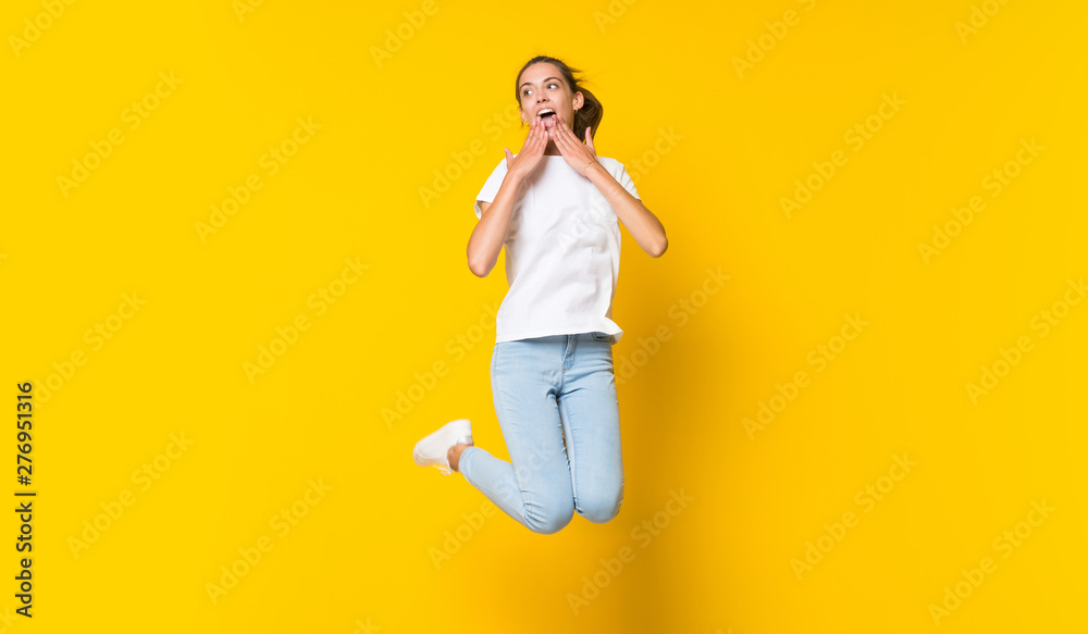Young woman jumping over isolated yellow wall Young woman jumping over isolated yellow wall