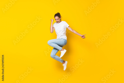Young woman jumping over isolated yellow wall