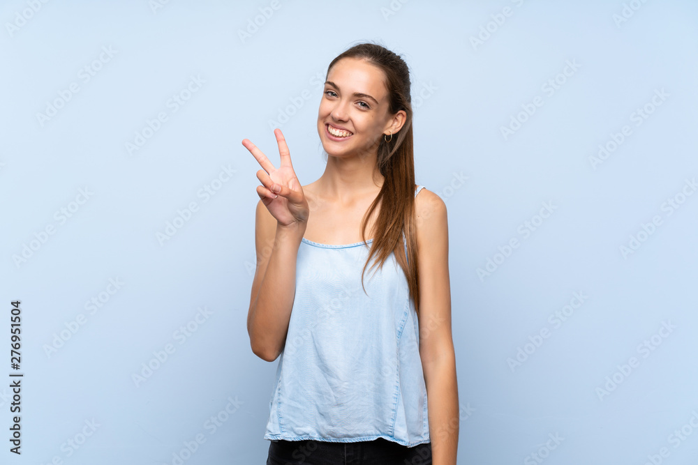 Young woman over isolated blue background smiling and showing victory sign Young woman over isolated blue background smiling and showing victory sign