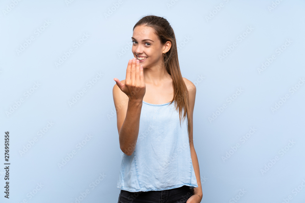 Young woman over isolated blue background inviting to come with hand. Happy that you came Young woman over isolated blue background inviting to come with hand. Happy that you came