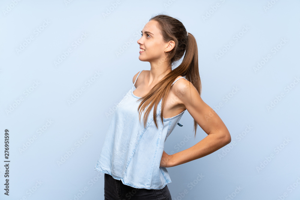Young woman over isolated blue background suffering from backache for having made an effort Young woman over isolated blue background suffering from backache for having made an effort