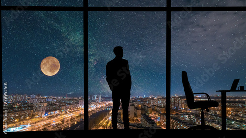 The man standing near the panoramic window on city with starry sky background © realstock1