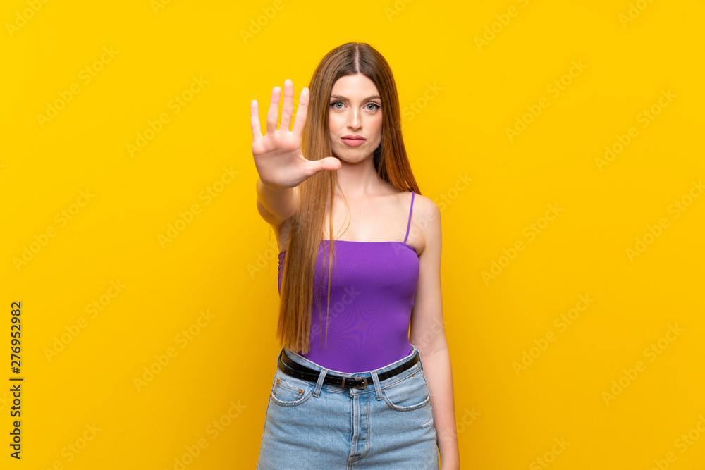 Young woman over isolated yellow background making stop gesture Young woman over isolated yellow background making stop gesture