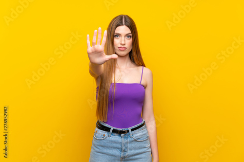 Young woman over isolated yellow background making stop gesture