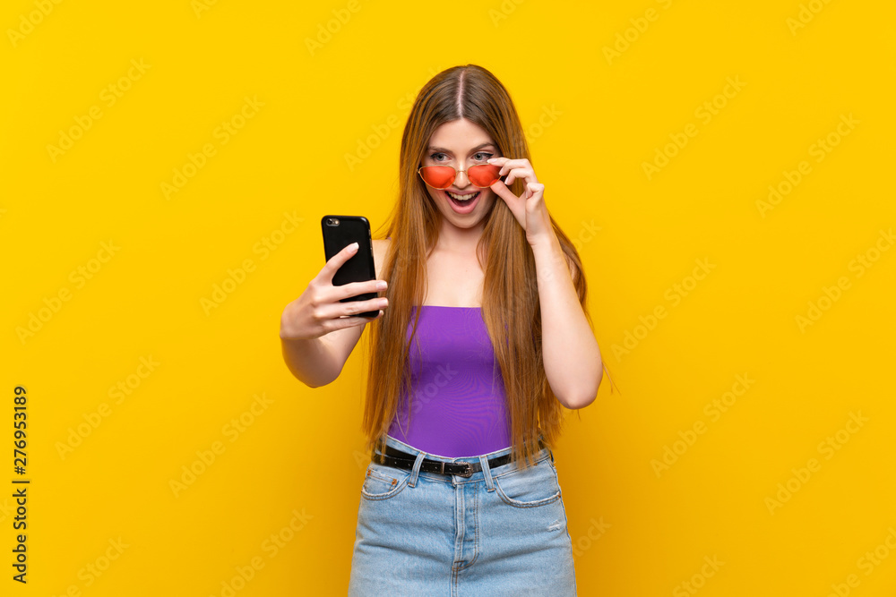 Young woman over isolated yellow background making a selfie Young woman over isolated yellow background making a selfie