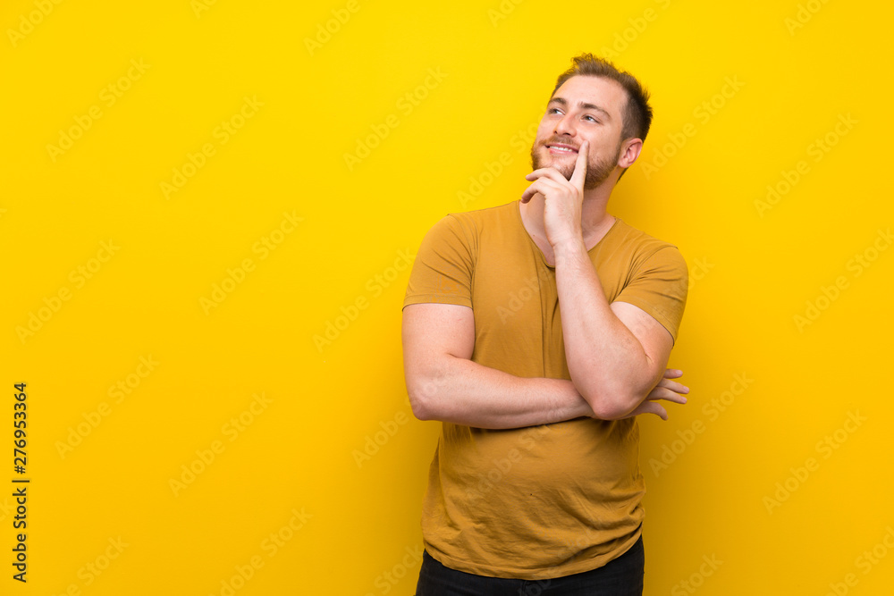Blonde man over isolated yellow wall thinking an idea while looking up Blonde man over isolated yellow wall thinking an idea while looking up