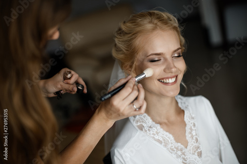 A bride is laughing while a makeup artist is putting a makeup on her face. photo