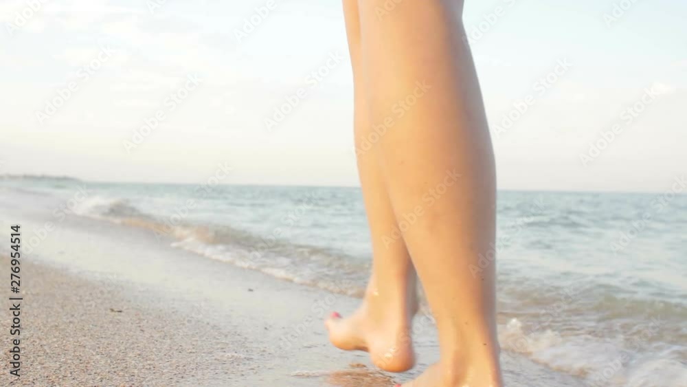 Point of view of young woman stepping at the golden sand at sea beach. Female legs walking near ocean. Bare foot of girl going on sandy shore with waves. Summer vacation or holiday Slow motion Closeup Point of view of young woman stepping at the golden sand at sea beach. Female legs walking near ocean. Bare foot of girl going on sandy shore with waves. Summer vacation or holiday Slow motion Closeup