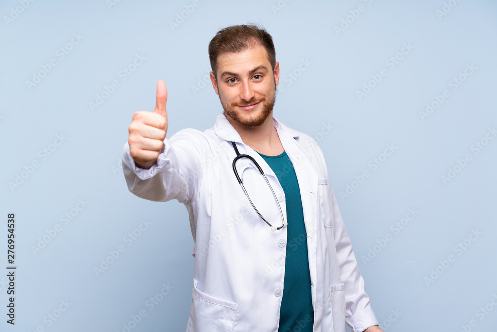 Handsome doctor man over blue wall with thumbs up because something good has happened Handsome doctor man over blue wall with thumbs up because something good has happened