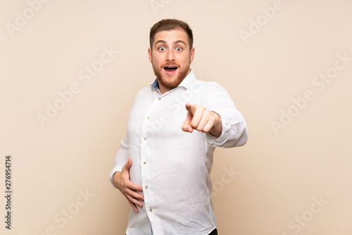 Blonde man over isolated background surprised and pointing front