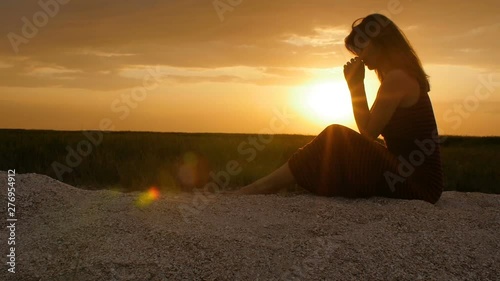 silhouette of a young woman on the sand at sunset, girl bowed her head in prayer to the Creator with gratitude, the concept of rest, religion, the beauty of nature and harmony