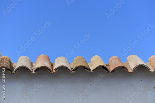 A white wall covered by roof tiles in front of a blue background.