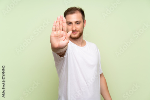 Handsome man over green background making stop gesture with her hand