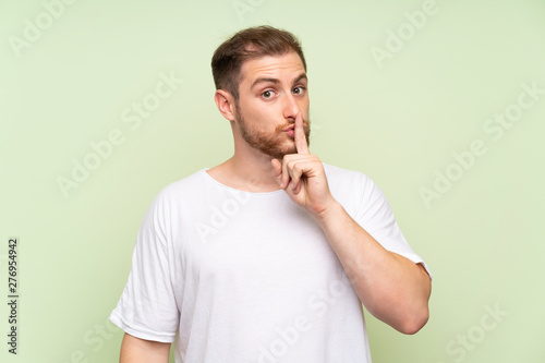 Handsome man over green background doing silence gesture