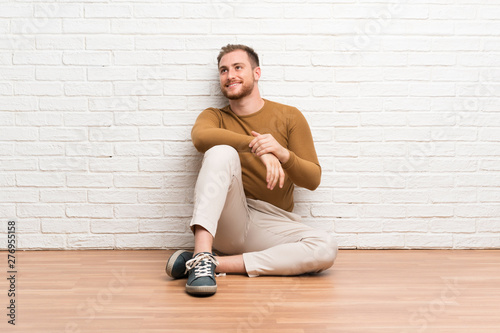 Blonde man sitting on the floor laughing and looking up