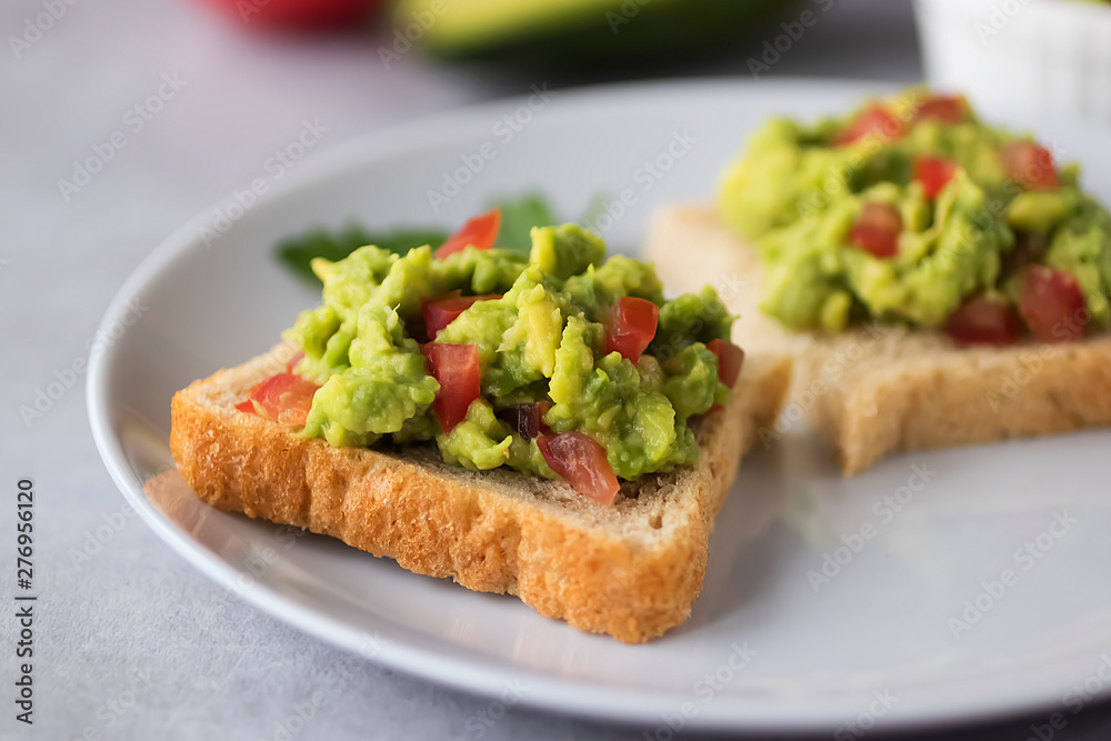 Toasts with an avocado snack and fresh vegetables on a gray background.