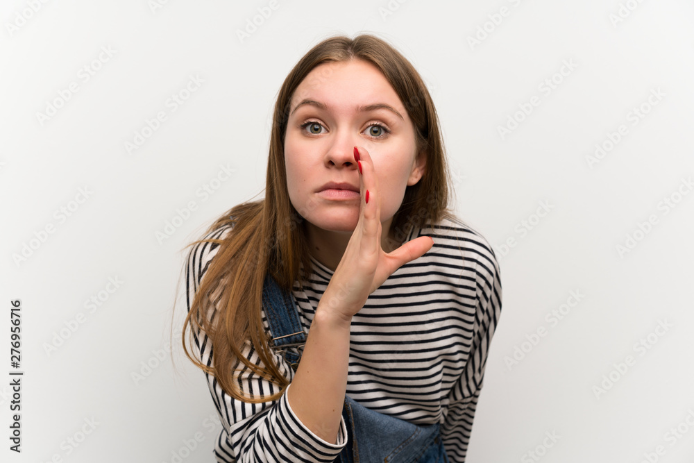 Young woman in dungarees over white wall whispering something Young woman in dungarees over white wall whispering something