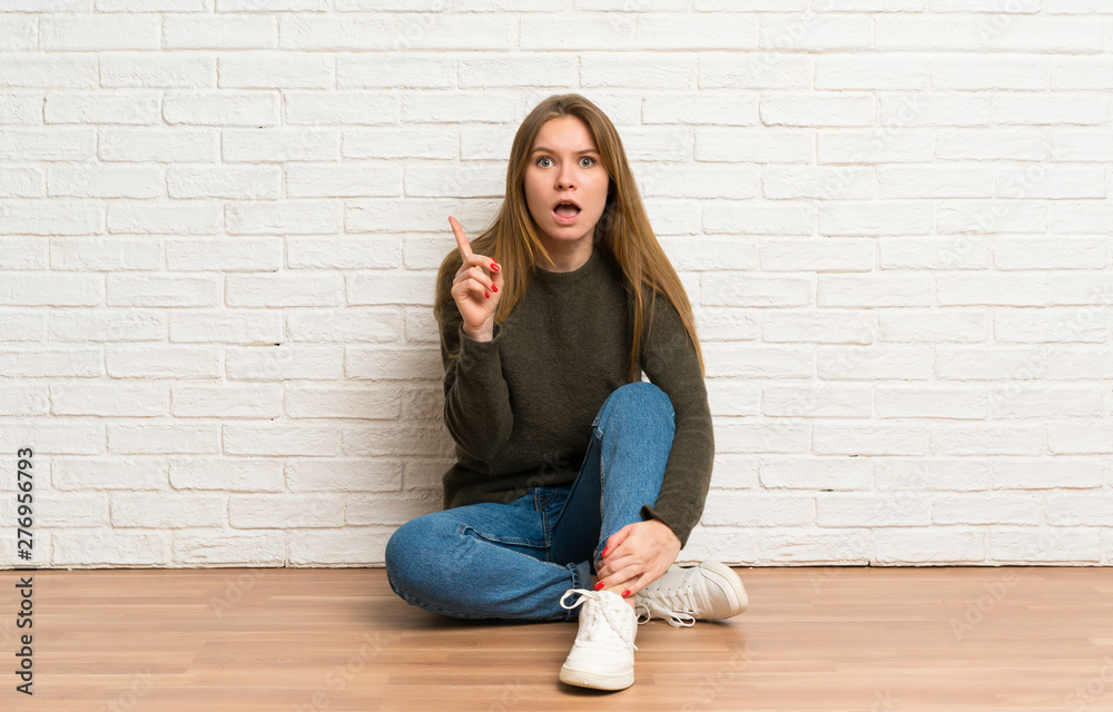 Young woman sitting on the floor thinking an idea pointing the finger up Young woman sitting on the floor thinking an idea pointing the finger up
