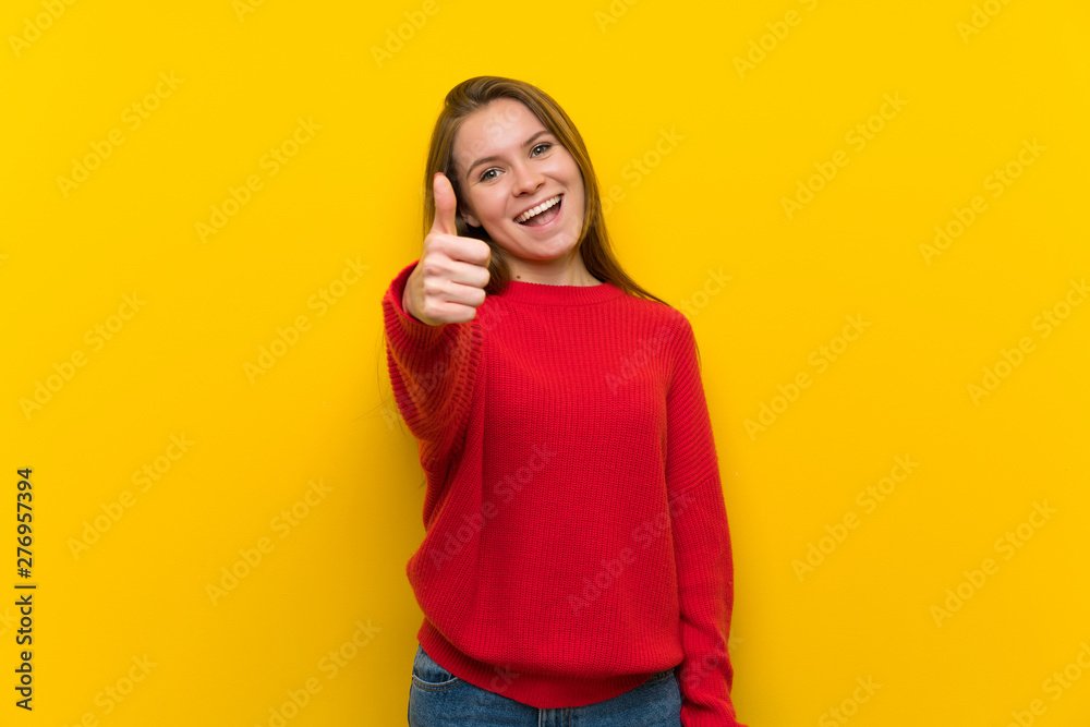 Young woman over yellow wall with thumbs up because something good has happened Young woman over yellow wall with thumbs up because something good has happened
