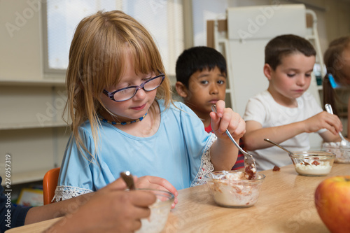 Young Multi Ethnic Kids Having Lunch Together At School. Kids Having Yogurt And Jello.