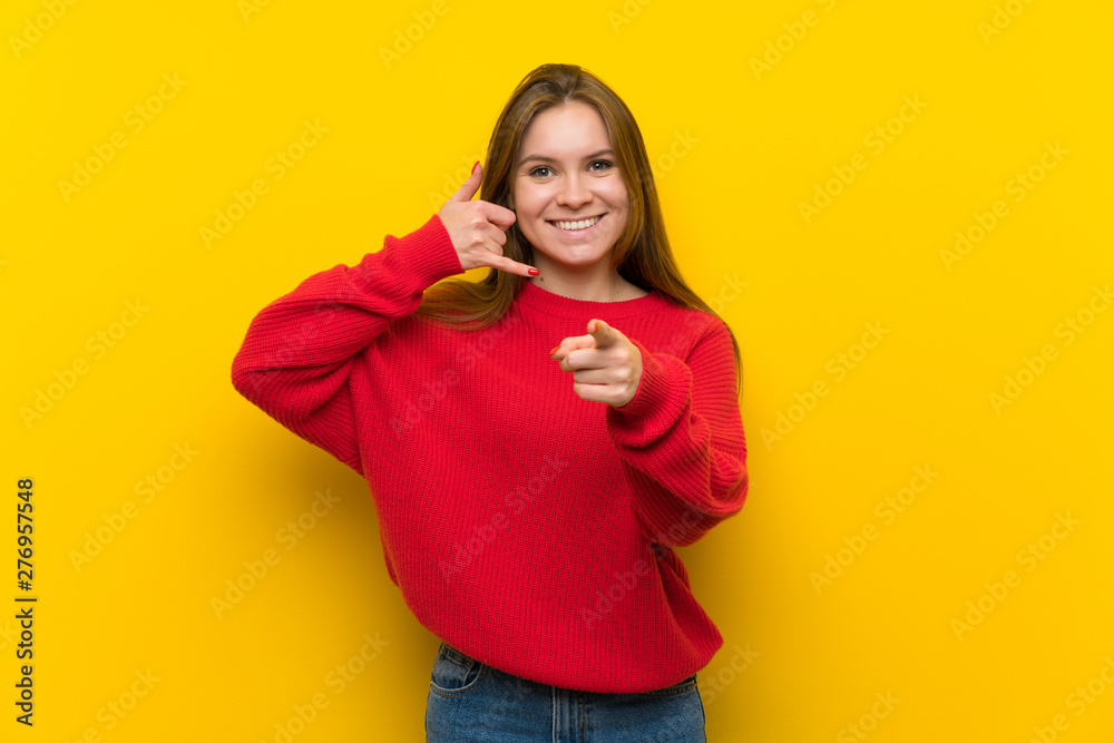 Young woman over yellow wall making phone gesture and pointing front Young woman over yellow wall making phone gesture and pointing front