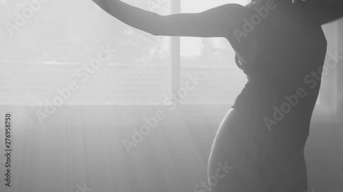 Silhouette of beautiful sensual woman in body suit dancing in hazy studio over window view background - black and white video in slow motion