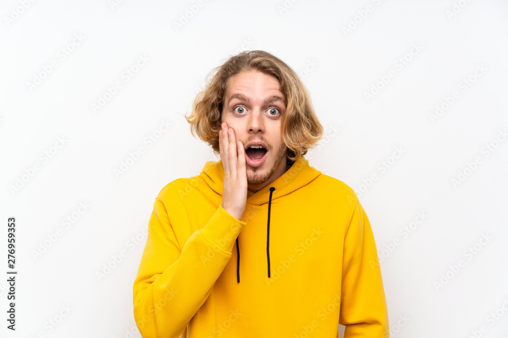 Blonde man with sweatshirt over white wall with surprise and shocked facial expression Blonde man with sweatshirt over white wall with surprise and shocked facial expression