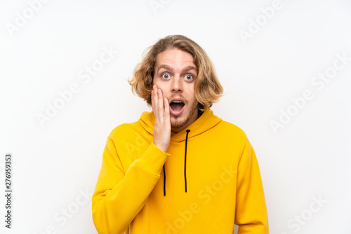 Blonde man with sweatshirt over white wall with surprise and shocked facial expression