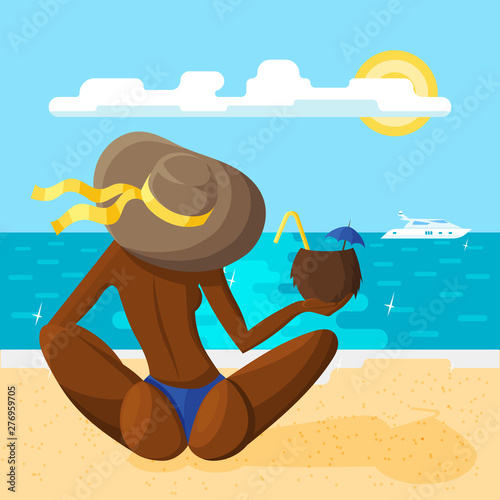 A young woman in a hat sits on the sandy beach with her back to the viewer with a coconut cocktail in her hand
