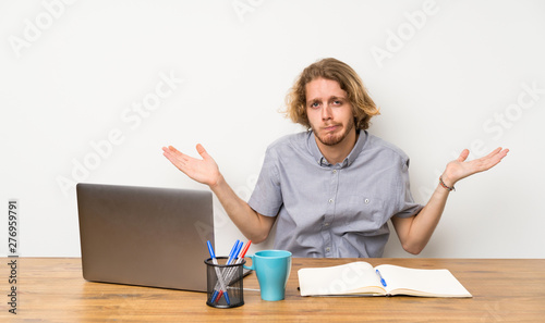 Blonde man with a laptop having doubts while raising hands © luismolinero