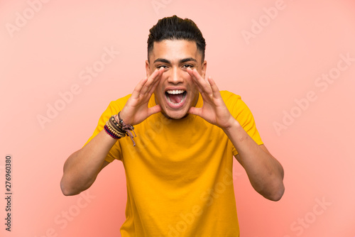 Young man with yellow shirt over isolated pink wall shouting with mouth wide open © luismolinero