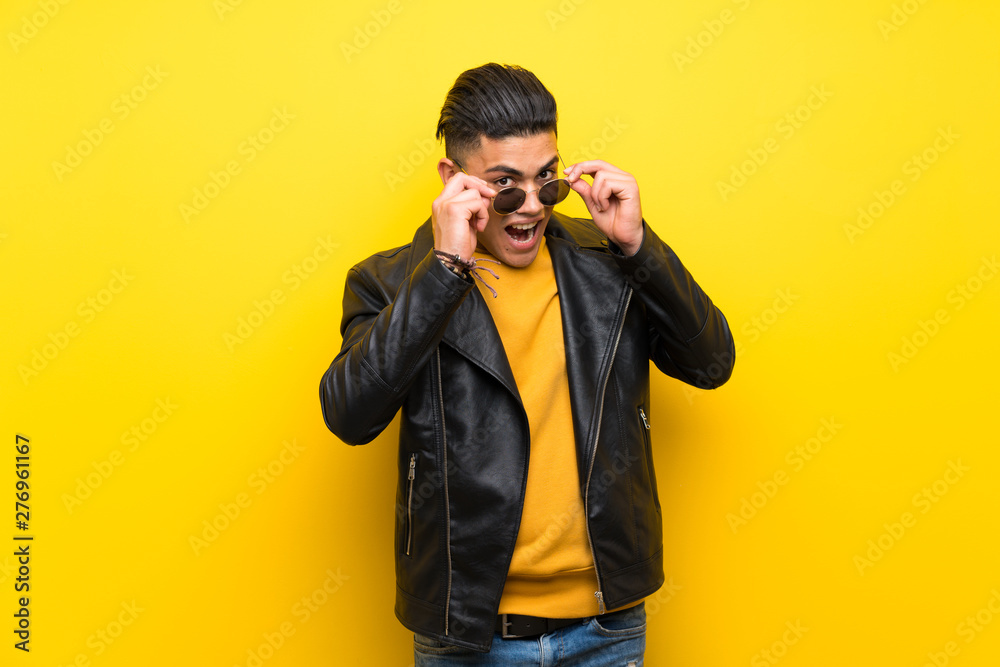Young man over isolated yellow background with glasses and surprised Young man over isolated yellow background with glasses and surprised