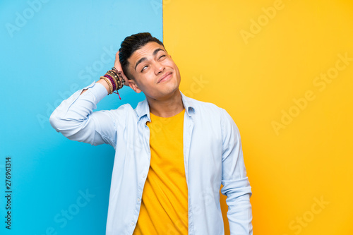 Young man over isolated colorful background having doubts and with confuse face expression