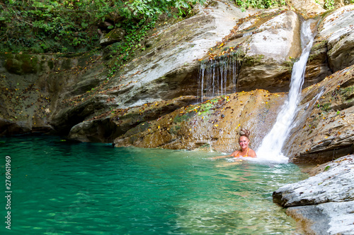 Pretty woman bathes in a mountain lake with waterfalls in the gorge Ahtsu area of Sochi, Russia.