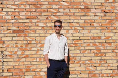 Portrait of a casually dressed young businessman standing against a brick wall
