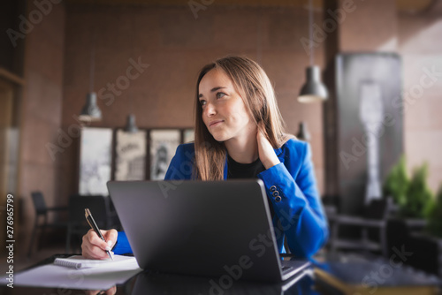 Beautiful business woman with a laptop and notebook looks thoughtfully