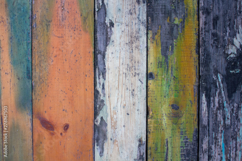 old gray wooden wall fence of multi-colored boards with peeling white, green and red paint. vertical lines. rough surface texture