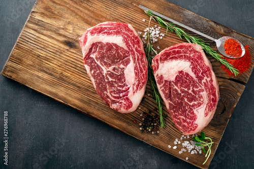 Two raw rib eye steak on the butcher's Board on a wooden table prepared prepared for cooking. Marbled beef top view