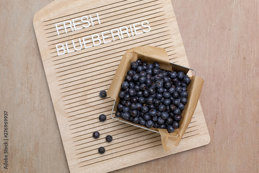 Freshly picked blueberries in small produce basket on letterboard. Letterboard says Freshly picked blueberries in small produce basket on letterboard. Letterboard says
