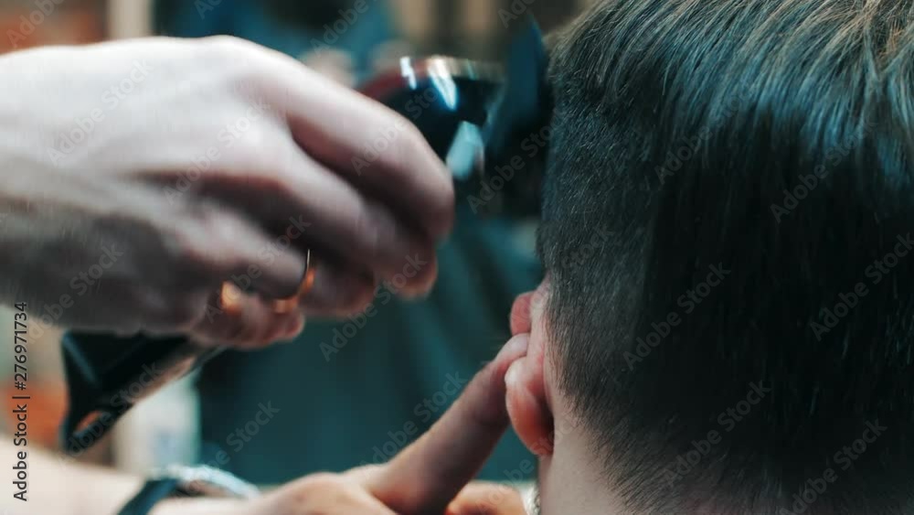 Barber making hairdo to man using electric clipper machine in barbershop Barber making hairdo to man using electric clipper machine in barbershop
