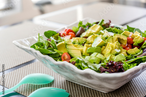 Natural vegetable salad rich in vitamins and fiber from green leaves and tomato and avocado in a ceramic dish