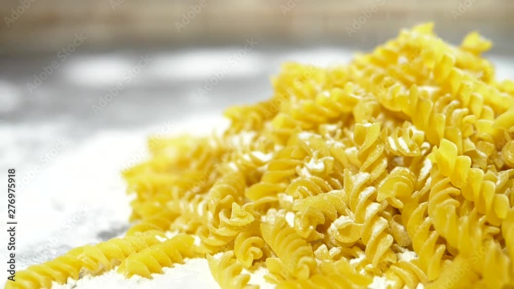 raw pasta fusilli, closeup lie in white flour on a wooden table. raw pasta fusilli, closeup lie in white flour on a wooden table.