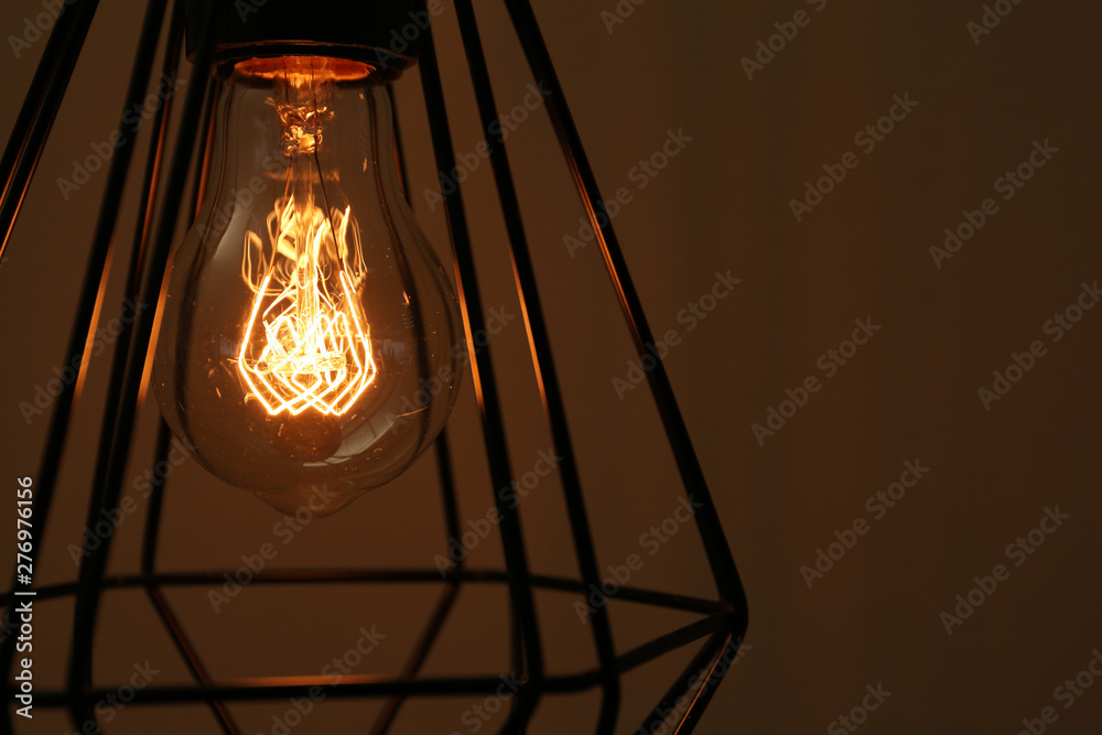 Hanging lamp bulb in chandelier against brown background, closeup