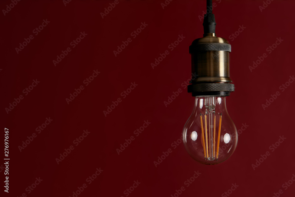Pendant lamp with light bulb against dark red background, space for text Pendant lamp with light bulb against dark red background, space for text