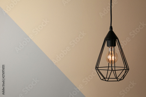 Hanging lamp bulb in chandelier against color background, space for text