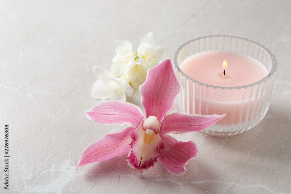 Lit candle and beautiful flowers on grey marble table. Space for text