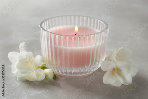 Lit candle and beautiful flowers on grey marble table