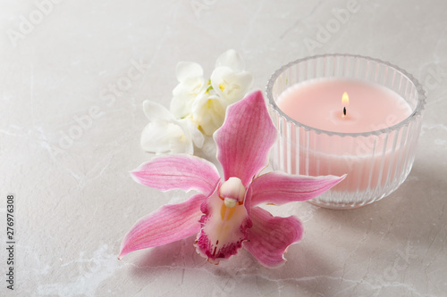 Lit candle and beautiful flowers on grey marble table. Space for text