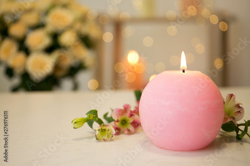 Burning candle and fresh flowers on table against blurred background. Space for text