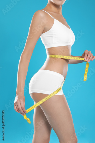 Slim young woman with smooth gentle skin in underwear measuring body on color background